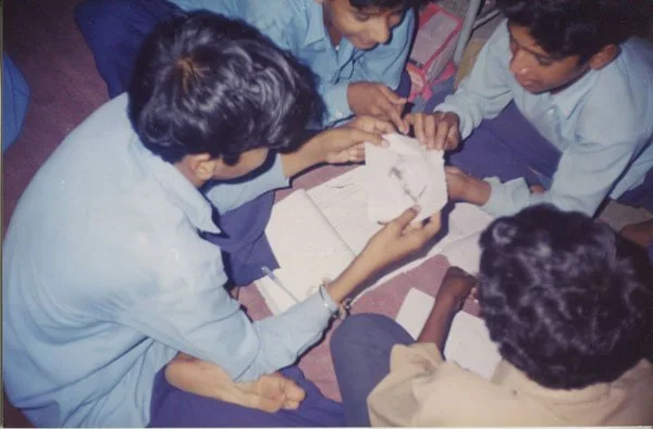 चार बच्चे फर्श पर चुंबक और लोहे के कणों का प्रयोग करते हुए।